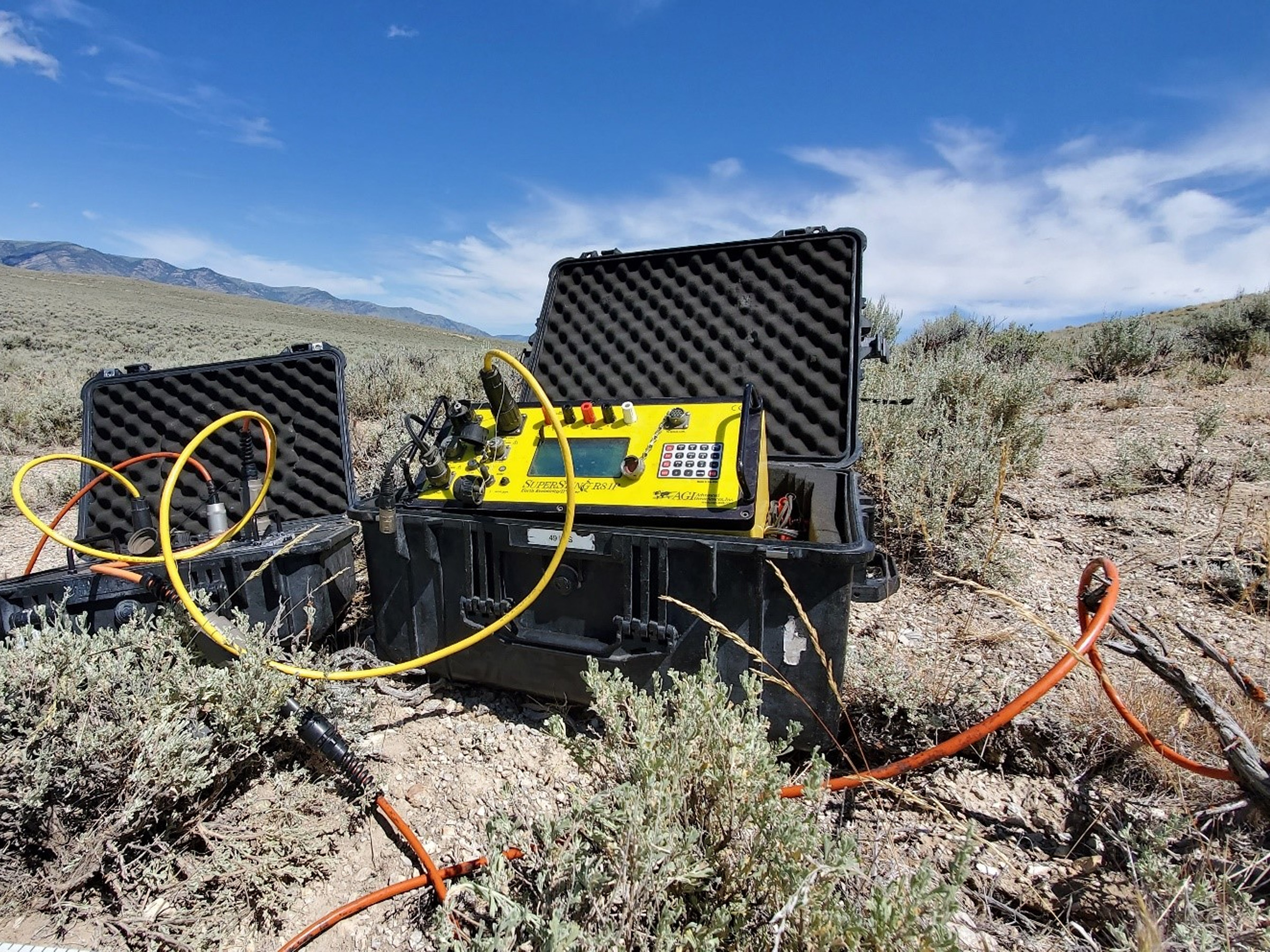 SuperSting R8 cihazı, kurak ve açık arazide taşınabilir saha kutusu içerisinde kurulu halde, çevresine yayılmış sarı ve turuncu kablolarla birlikte aktif ölçüm pozisyonunda görüntüleniyor. Cihazın saha adaptasyonu ve mobil kurulum yetenekleri bu geniş açılı karede net biçimde gözlemleniyor.